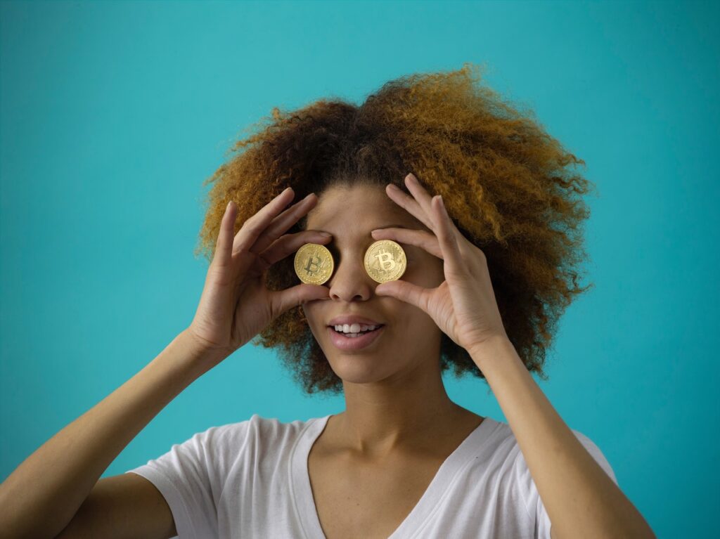 woman holding two Bitcoins up over her eyes